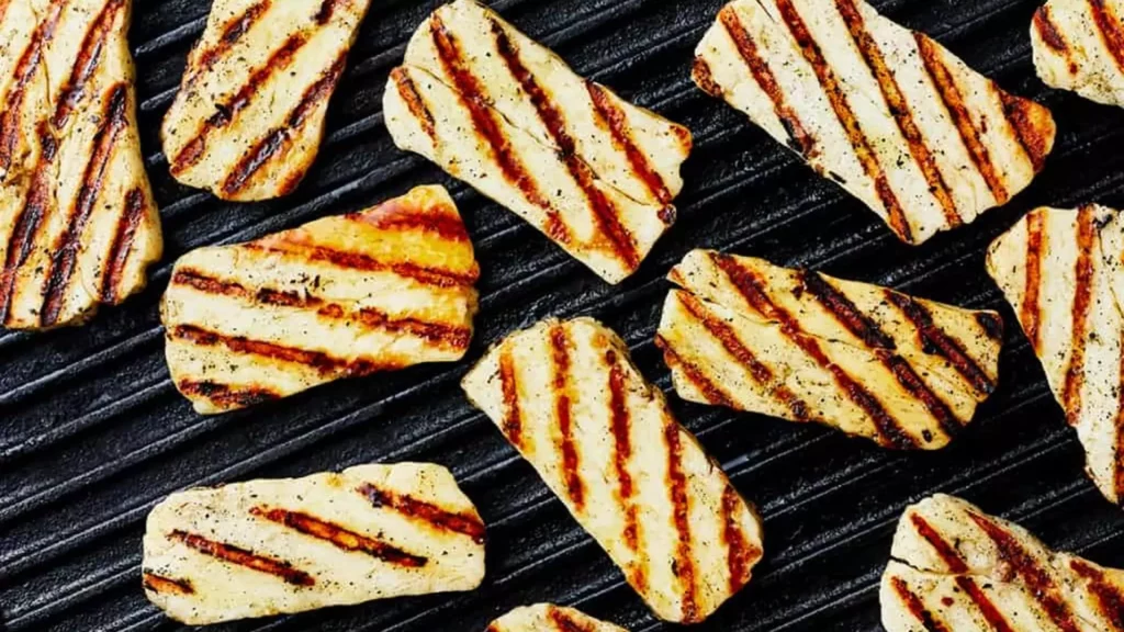 Grilled halloumi cheese slices arranged on a wooden board, garnished with fresh herbs and drizzled with olive oil