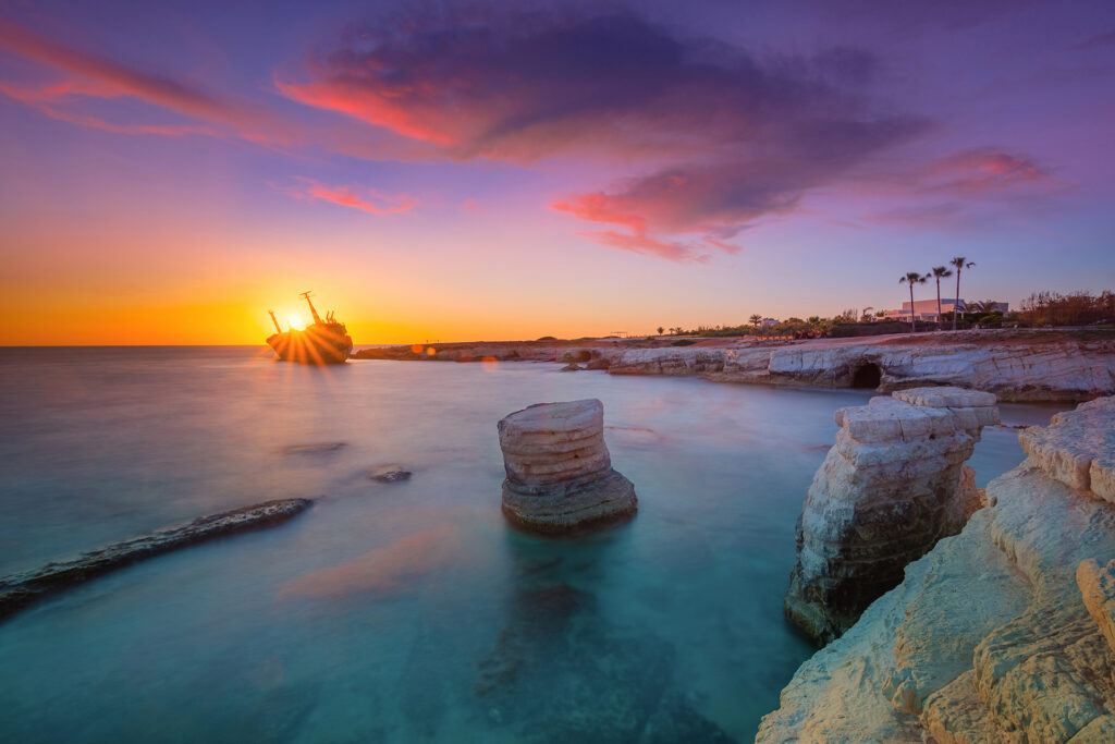 Seaside view of Oniro by the Sea in Peyia, Cyprus, during a vibrant sunset with the sky glowing orange and pink.