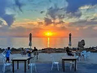 Yialos Tavern in Coral Bay, featuring outdoor seating with a view of the sea, surrounded by vibrant greenery