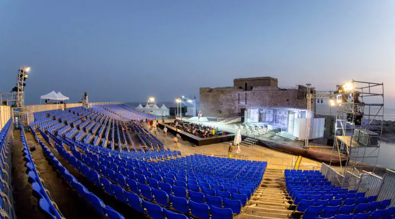 Open-air seating and illuminated stage beside Paphos Medieval Castle, prepared for the Pafos Aphrodite Festival.