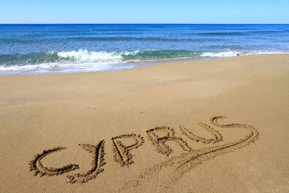 Crystal-clear turquoise waters gently lapping against a sandy beach in Cyprus, with a bright blue sky overhead.