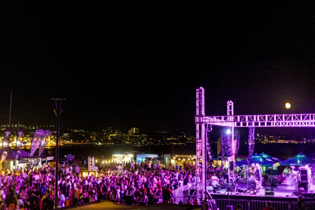 Group of festivalgoers dancing and enjoying live music at the Paphos Beer Festival, surrounded by colorful decorations and vibrant atmosphere.