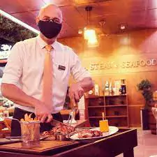Photo of a succulent steak being carved at the table at Andria's Steak and Seafood restaurant, showcasing a perfectly cooked piece of meat with garnishes.