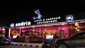 Photo of the outdoor terrace at Andria's Steak and Seafood restaurant, featuring wooden patio furniture, colorful flower pots, and views of Coral Bay.