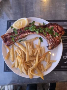 Jumbo pork chop served at Cousins Tavern in Peyia, plated with sides and garnishes on a restaurant table.
